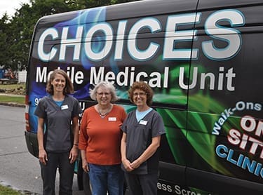 Choices Medical team members Leah DeHoyos (left) and Teri Nunnally (right) stand in front of the Mobile Medical Unit with Joyce Allen, a volunteer.
